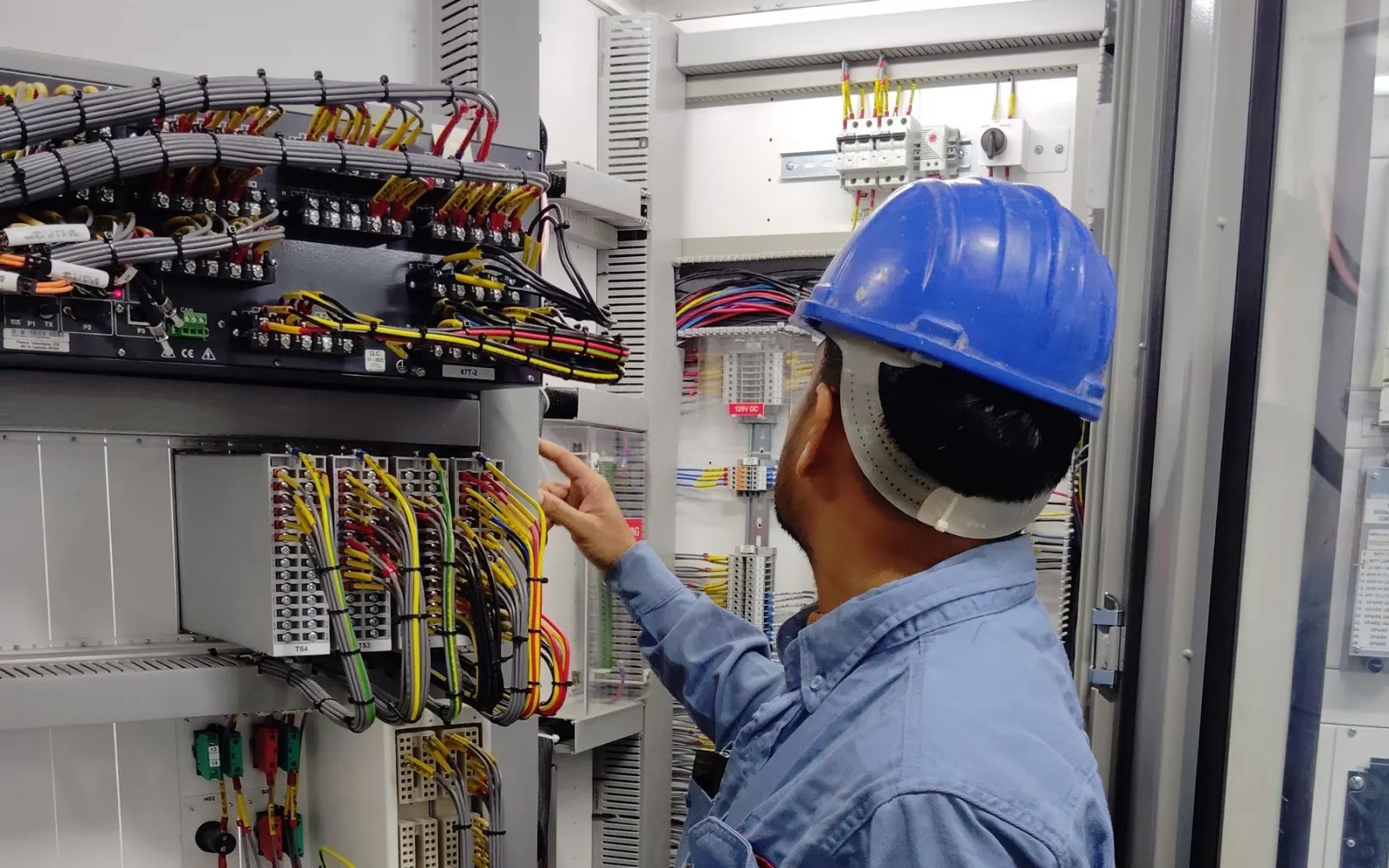 Baretli elektrik teknisyeninin pano içindeki kablo bağlantılarını kontrol etmesi